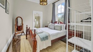 A bedroom with a wooden bed, a mirror, a hanging light fixture, a window with curtains, and a white storage unit.