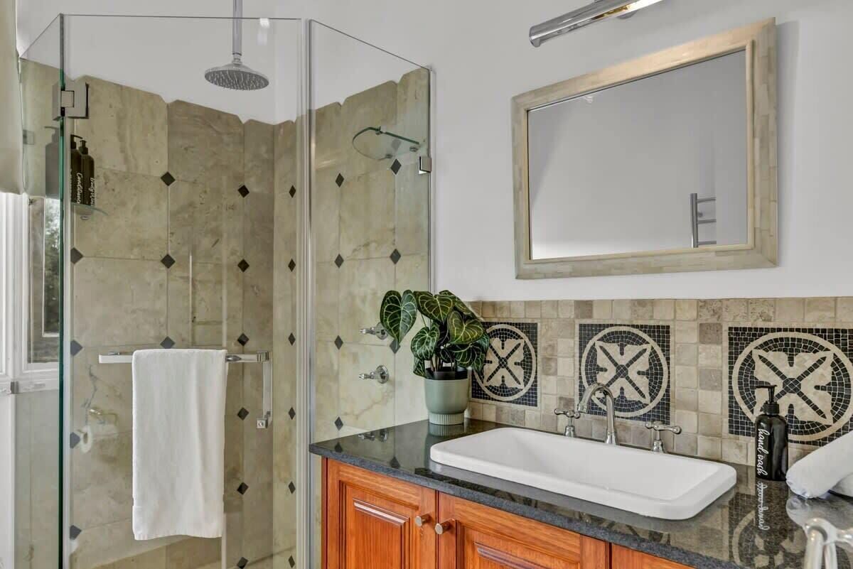 A modern bathroom with a glass shower enclosure, a white sink, wooden cabinets, and a large mirror.
