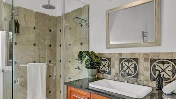 A modern bathroom with a glass shower enclosure, a white sink, wooden cabinets, and a large mirror.
