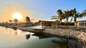 Un complexe hôtelier moderne doté d’une piscine, de palmiers et offrant une vue imprenable sur le coucher de soleil.