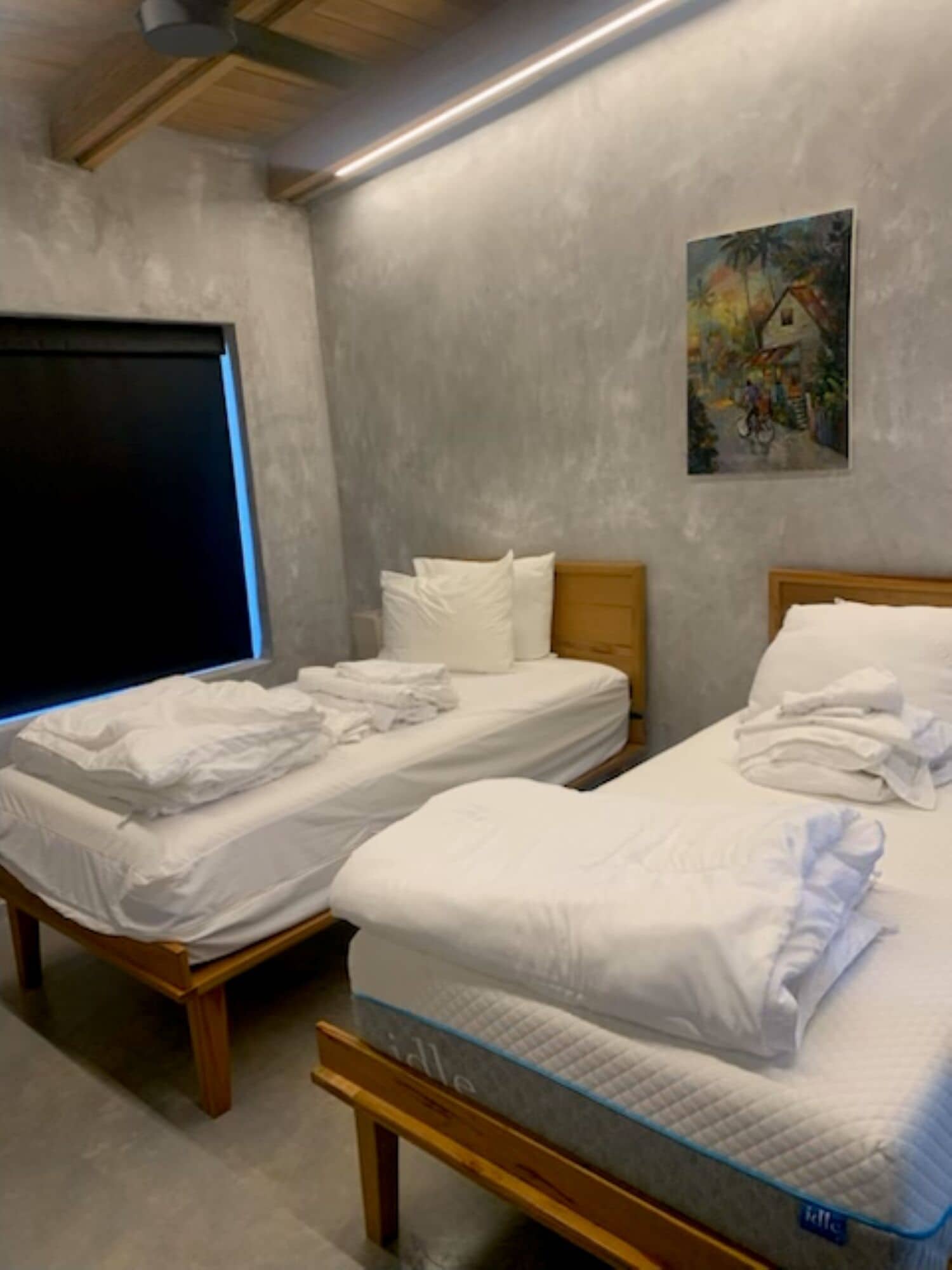 Ein Hotelzimmer mit zwei Einzelbetten, einem großen Fenster, einem Gemälde an der Wand und einer Decke mit Holzbalken.