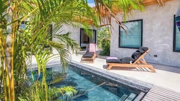 Un espace piscine moderne, doté de chaises longues et d’une piscine à eau claire, le tout entouré d’une végétation luxuriante.
