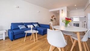 Un soggiorno moderno con un divano blu, un tavolo da pranzo rotondo con sedie bianche e una cucina sullo sfondo.