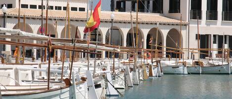 A marina with multiple boats docked, a building with arched windows, and a flag.