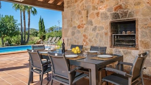 Un área de comedor al aire libre con muros de piedra, piscina y una parrilla.