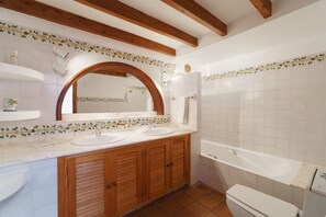 A bathroom with wooden cabinets, a double sink, a large mirror, and a bathtub. - Townhouse Calvario at Calvari (Pollensa / Pollença)