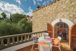 A stone building with a balcony, white wicker furniture, and a table with a tablecloth.