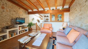Una sala de estar acogedora con techo de madera, paredes de piedra, televisor, estanterías, un sofá y una mesa de centro.
