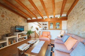 A cozy living room with a wooden ceiling, stone walls, a television, bookshelves, a sofa, and a coffee table.