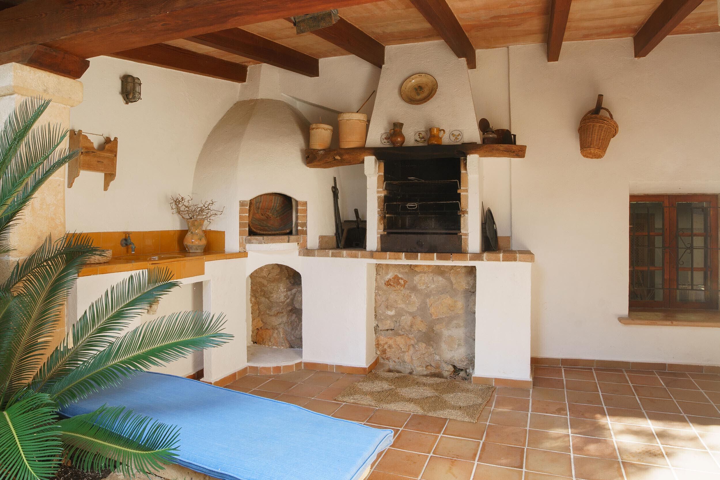 A rustic kitchen with a stone fireplace, wooden beams, and a blue mat on the floor.