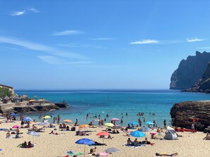 A crowded beach with people sunbathing and swimming, tents set up, and a rocky cliff in the background. - Townhouse Calvario at Calvari (Pollensa / Pollença)
