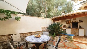 A patio with a round table, chairs, and a bowl of fruit. There is a stone wall, a potted plant, and a tiled floor. - Townhouse Calvario at Calvari (Pollensa / Pollença)