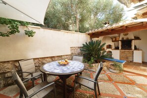 A patio with a round table, chairs, and a bowl of fruit. There is a stone wall, a potted plant, and a tiled floor. - Townhouse Calvario at Calvari (Pollensa / Pollença)