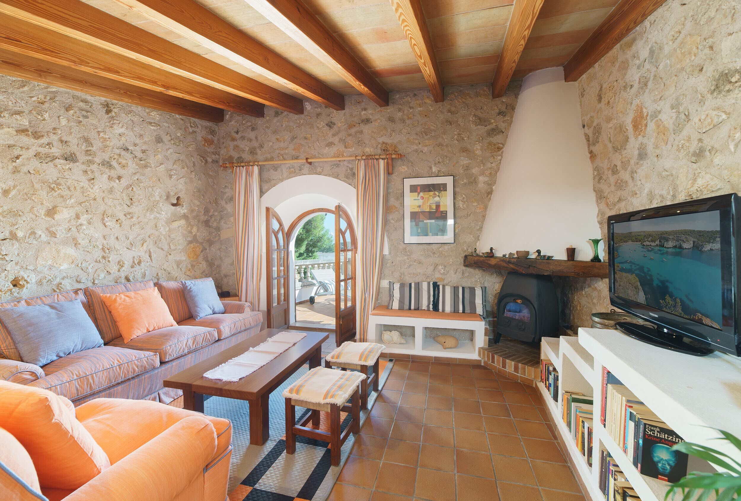 A cozy living room with a stone wall, wooden beams, a sofa, a coffee table, a fireplace, and a television.