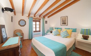 A bedroom with a large bed, a wooden ceiling, a window with curtains, a chair, a desk with a lamp, and a painting on the wall. - Townhouse Calvario at Calvari (Pollensa / Pollença)
