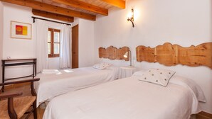 Una habitación con dos camas, vigas de madera en el techo, una lámpara de pared y una ventana con cortinas.