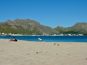 A beach with mountains in the background, a clear sky, and a few people.