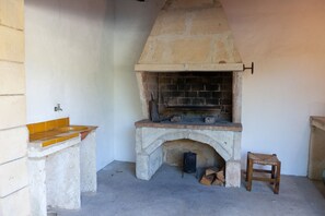 A stone-built fireplace with a brick interior, a small wooden stool, and a tiled bench.