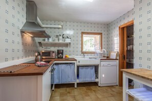 A compact kitchen with a microwave, toaster, and sink. There is a window providing natural light and a wooden cabinet above the sink. - Colonya Petit - Villa Majorca mieten (Pollensa / Pollença)