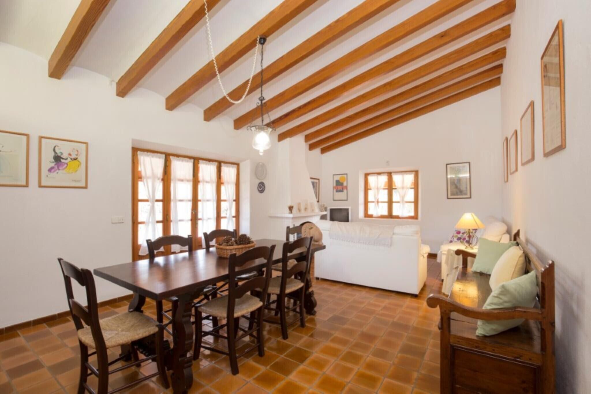 Ein Essbereich mit Holztisch und Stühlen, ein Küchenbereich mit weißer Arbeitsplatte und ein Wohnbereich mit Sofa und Lampe.