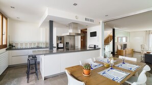 Una cocina moderna con una isla central, electrodomésticos de acero inoxidable y un comedor con mesa de madera y sillas blancas.