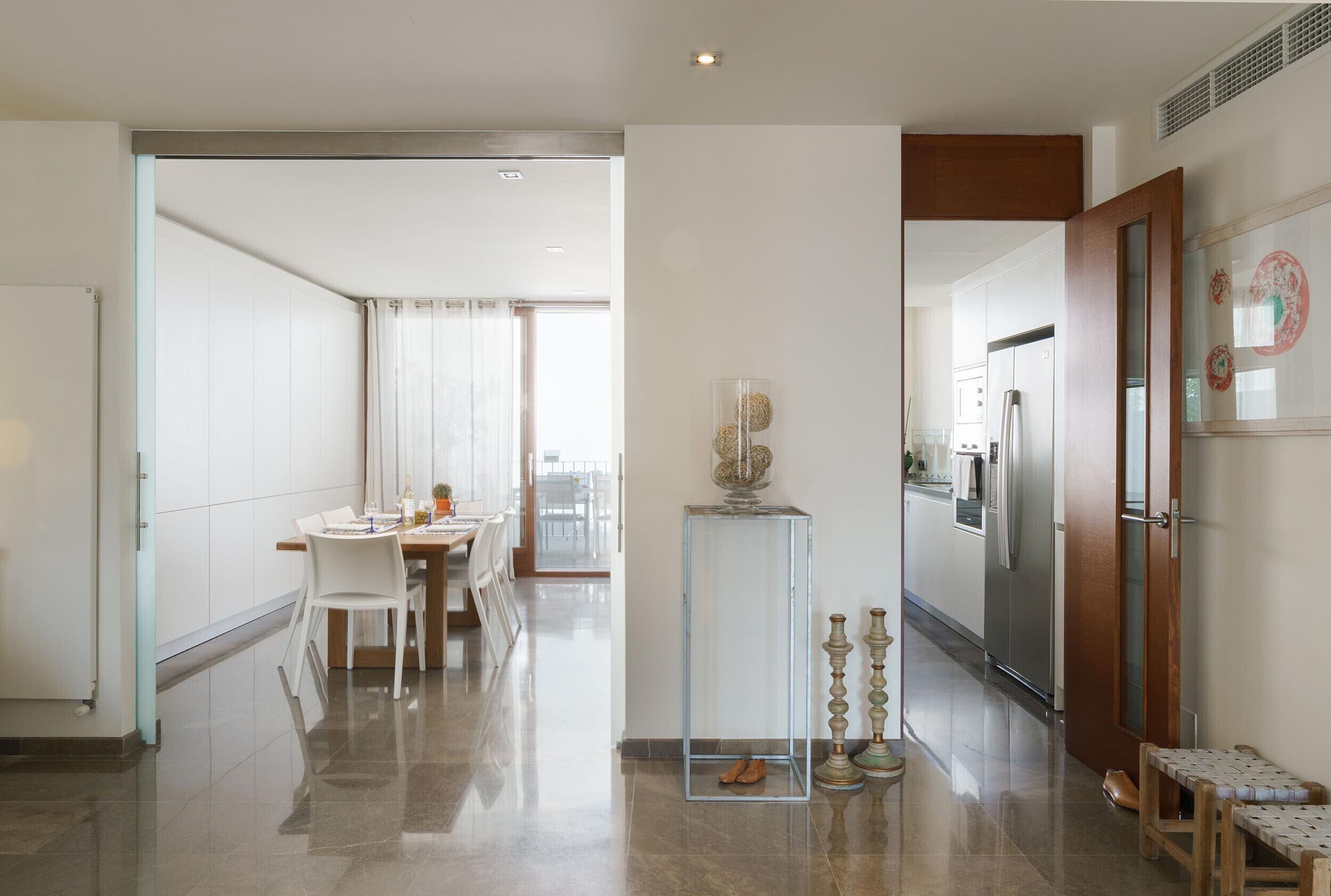 A modern kitchen with a refrigerator, a dining area with chairs, and a clear glass cabinet.