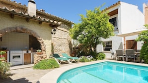 A pool with lounge chairs, a stone building with a chimney, and a kitchen area.