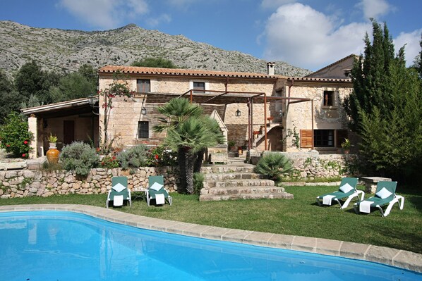 A stone villa with a swimming pool, outdoor seating, and a mountainous backdrop.