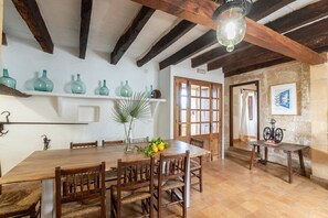 A dining area with a wooden table and chairs, a hanging light fixture, and a shelf with green vases.