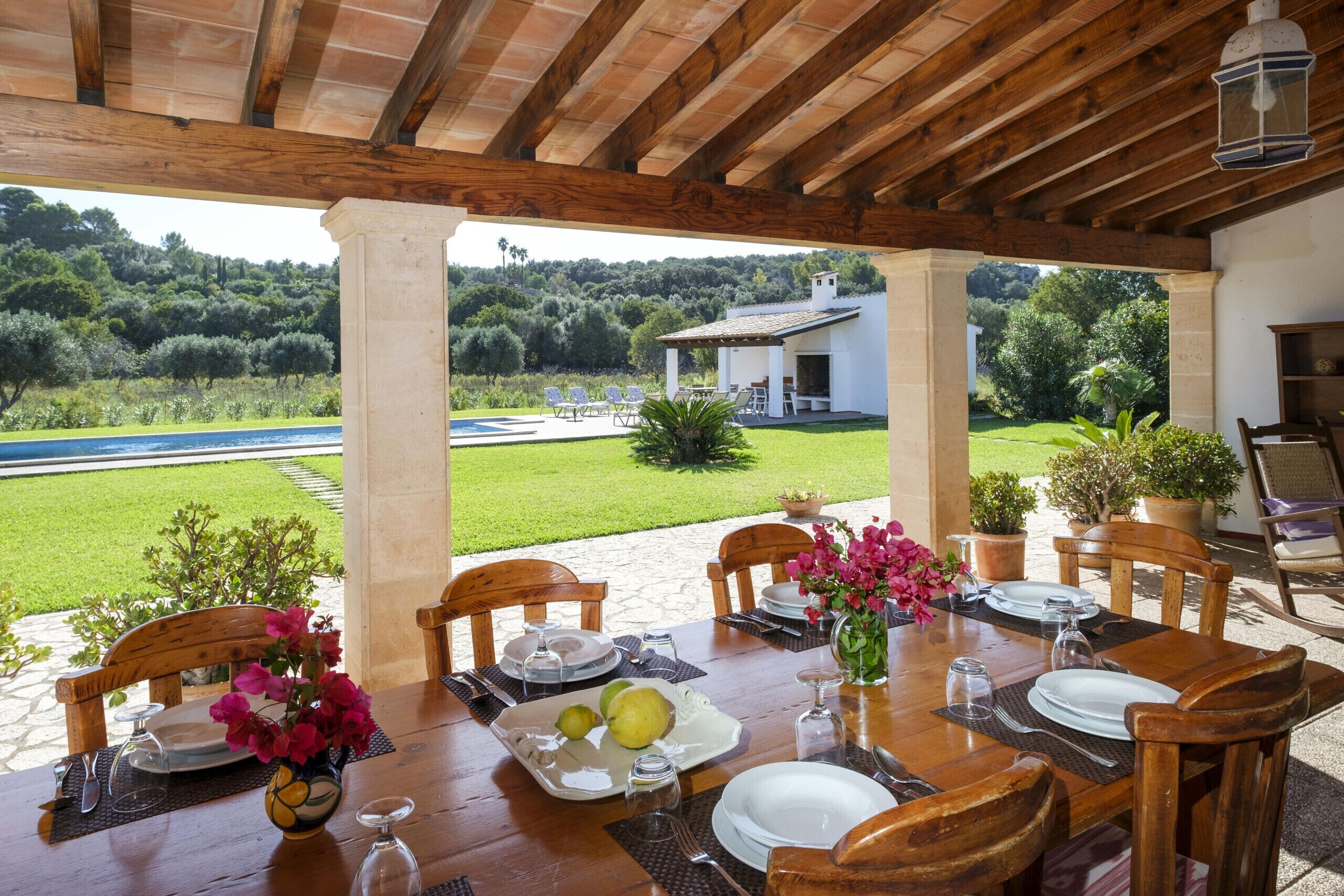 Un área de comedor al aire libre con vistas a un jardín exuberante y un edificio blanco al fondo.