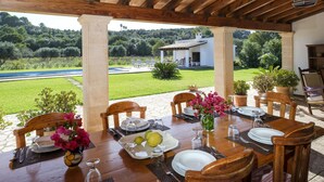 Uma área de refeições ao ar livre com vista para um jardim exuberante e um edifício branco ao fundo.