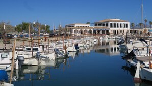 Uma marina com vários barcos atracados, um edifício com arcos e um céu azul límpido.