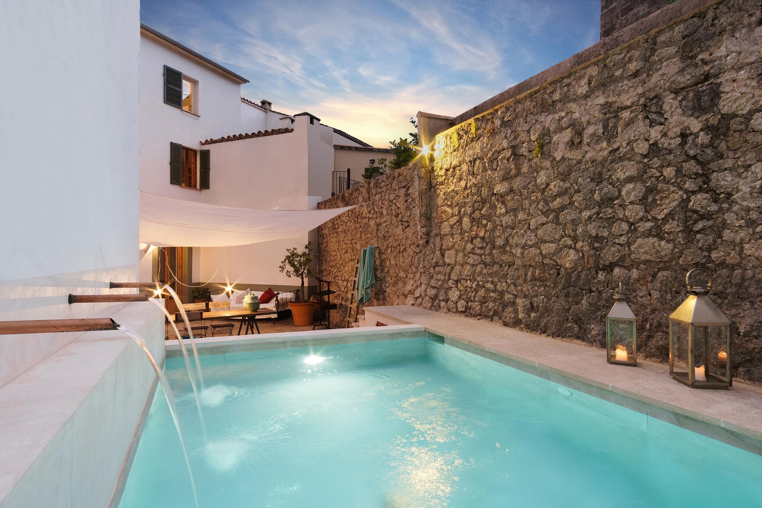 A swimming pool with a stone wall and a white building in the background.