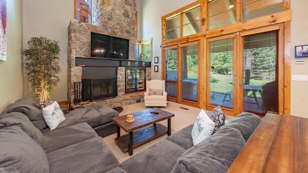 A spacious living room with a stone fireplace, large windows, and a cozy seating area. - Mountain Top Ski In/Out Chalet w/ Hot Tub (McHenry)