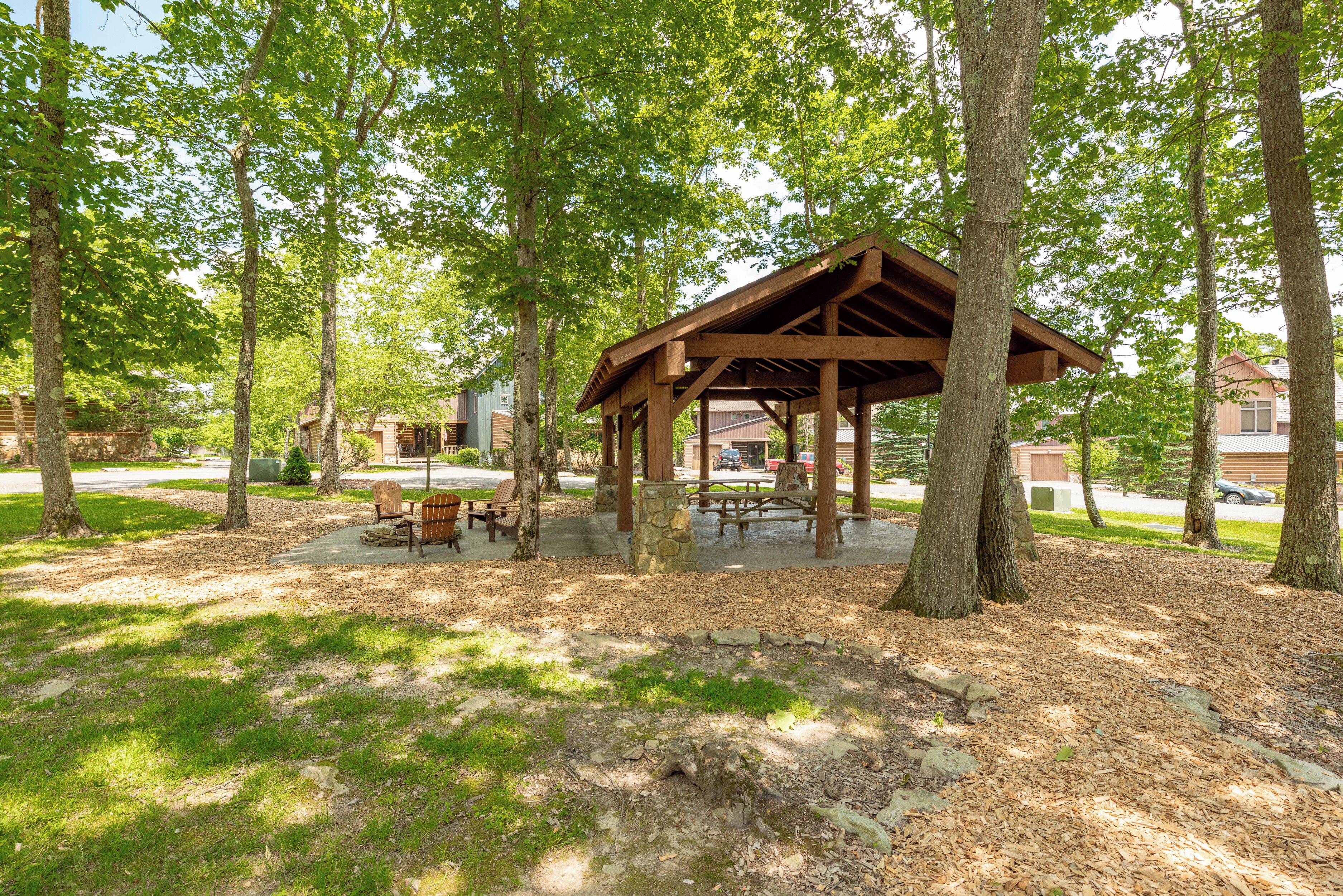A wooden pavilion with benches and picnic tables surrounded by trees.