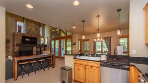 A spacious kitchen with a stone fireplace, wooden bar stools, a stainless steel dishwasher, and a large island with a sink. - Mountain Top Ski In/Out Chalet w/ Hot Tub (McHenry)