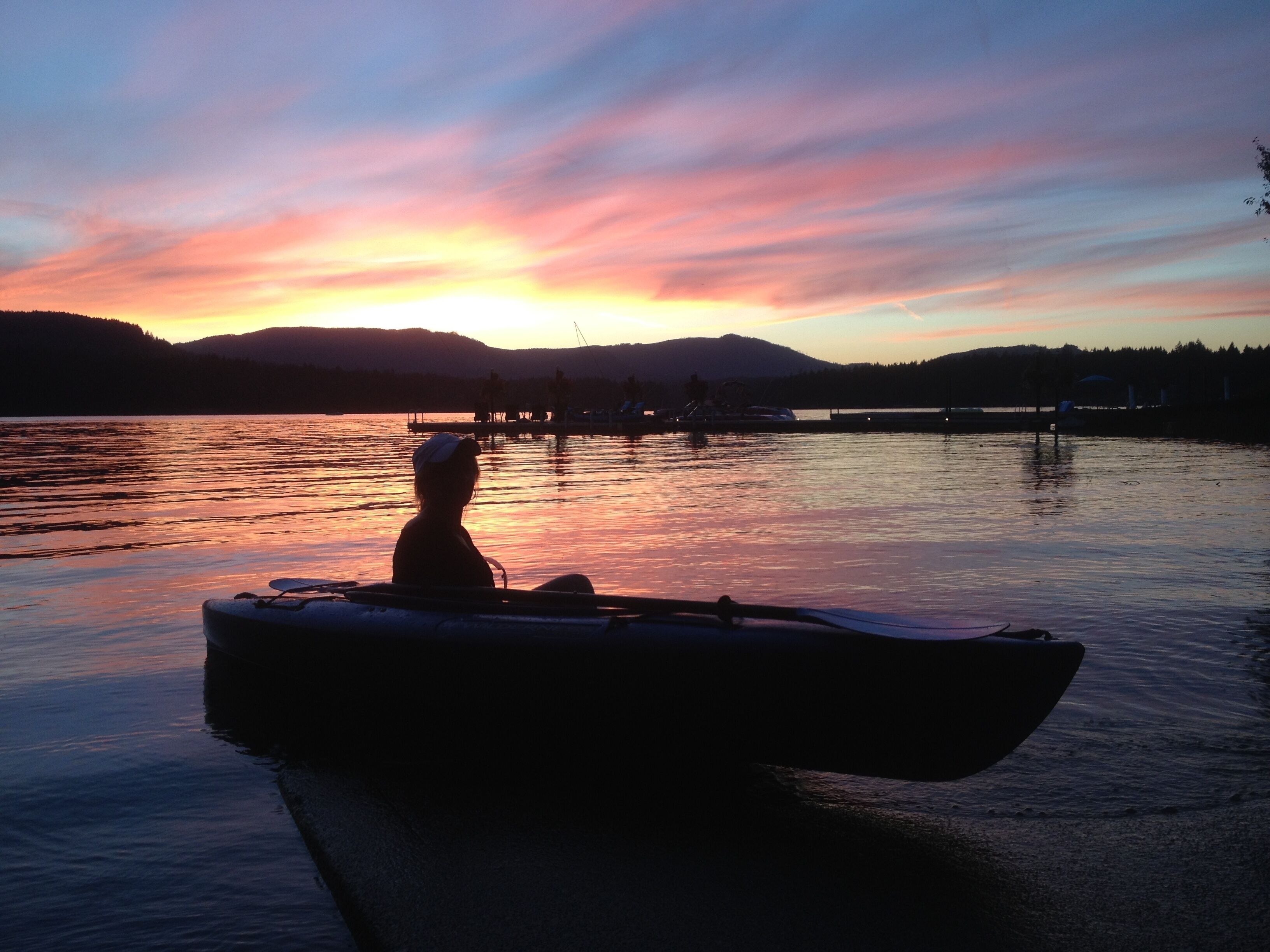 A boat on calm water during sunset with a silhouette of a person and a dog, surrounded by a natural landscape.