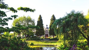 Un jardín tranquilo con un estanque, abundante vegetación y un edificio tradicional con una torre.