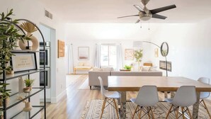 Una sala de estar moderna con comedor, ventilador de techo y estantería con plantas.