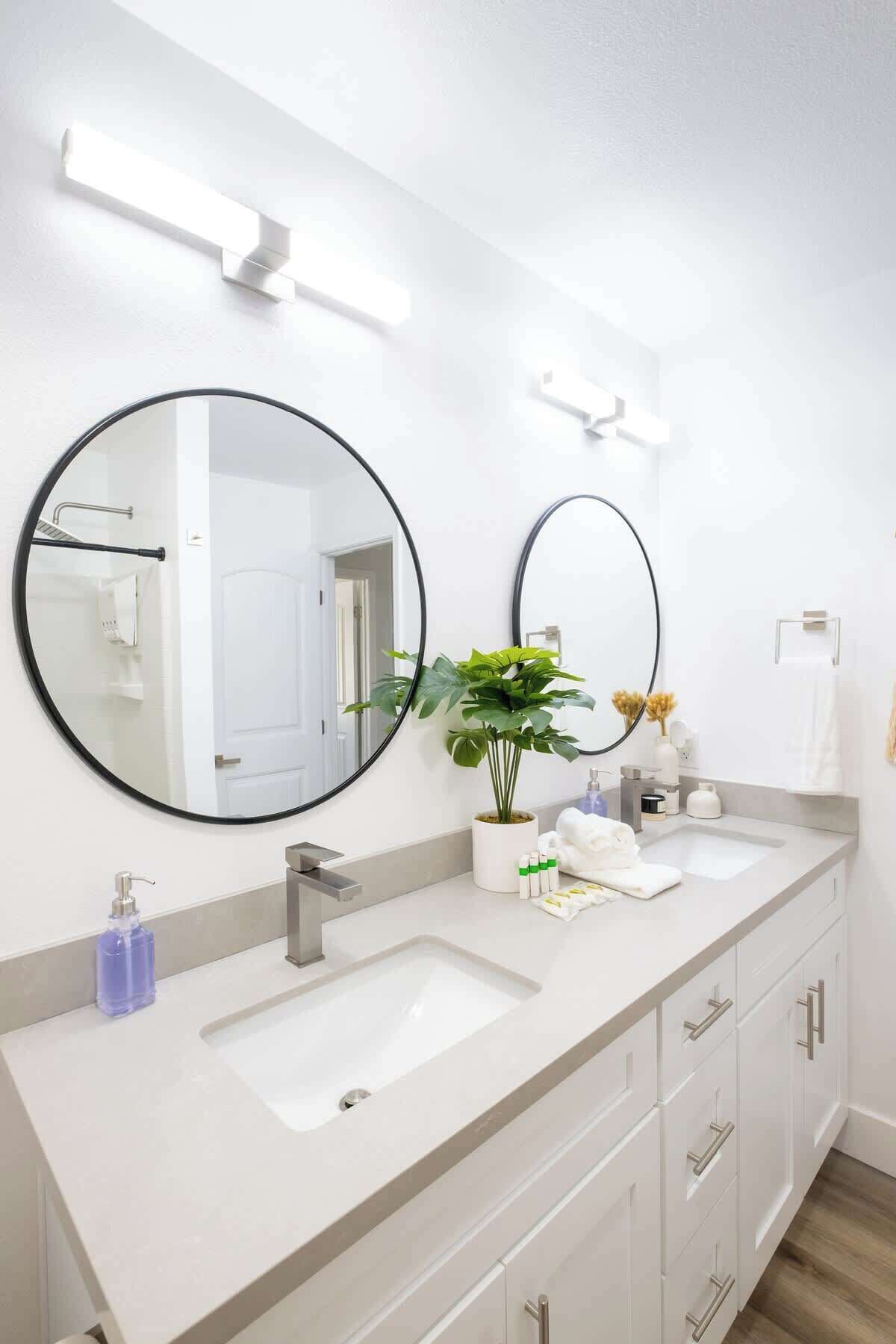 Un baño moderno con dos lavamanos, un espejo grande y una planta en maceta.