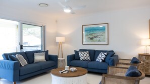Een moderne woonkamer met twee blauwe banken, een ronde salontafel en rieten stoelen.
