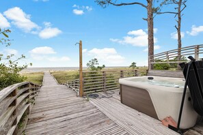 A wooden deck leading to a hot tub with a view of the beach.