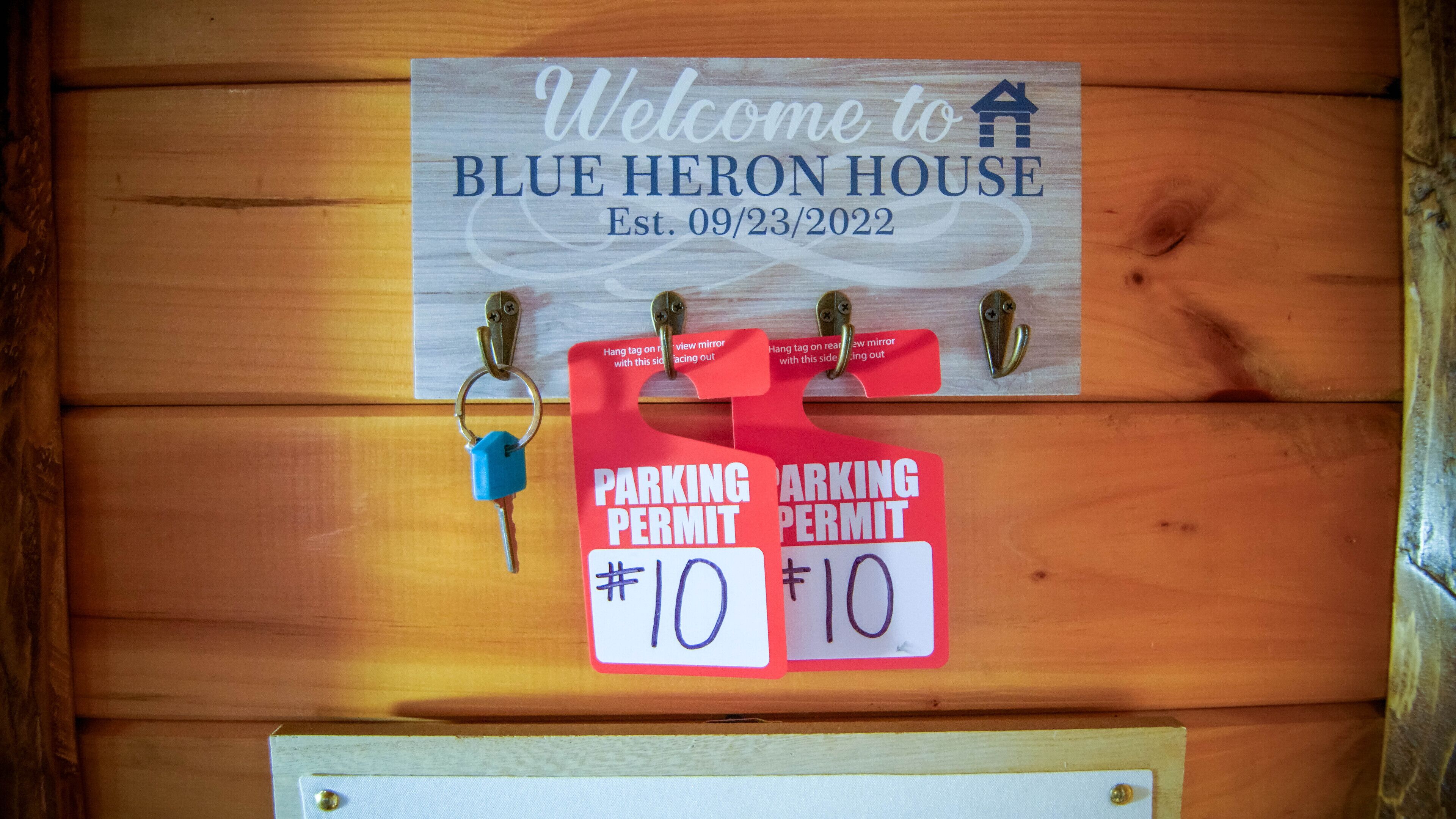 A wooden door with a welcome sign for Blue Heron House, established on 09/23/2022, and two red parking permit signs with the number 10.