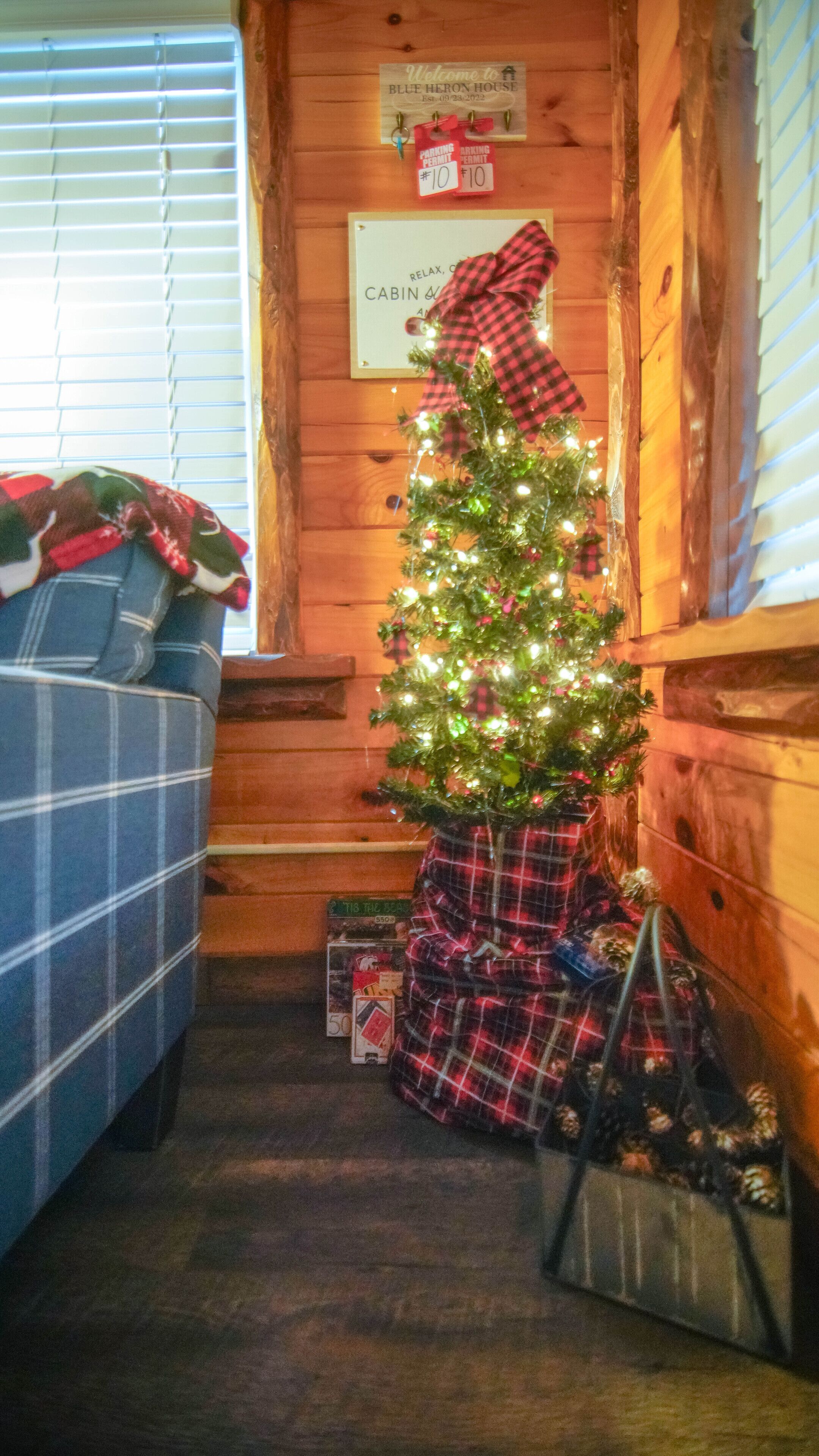 A cozy cabin interior with a decorated Christmas tree, plaid blankets, and a sign indicating a cabin rental.
