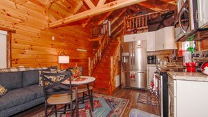 A cozy log cabin interior with a sofa, dining table, chairs, a kitchen with a refrigerator, stove, and coffee maker. - Charming Lakeview Cabin Near Geneva-On-The-Lake, The Perfect Getaway! (Ashtabula)