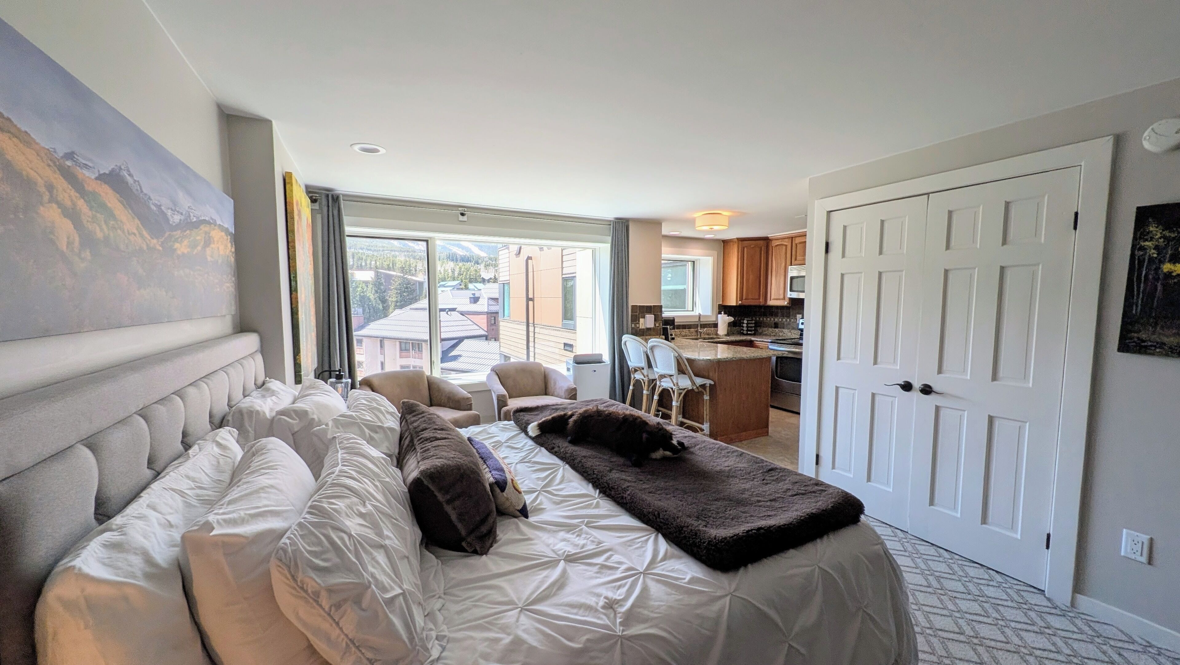 A hotel room with a bed, a sofa, a dining area, and a view of the outside.