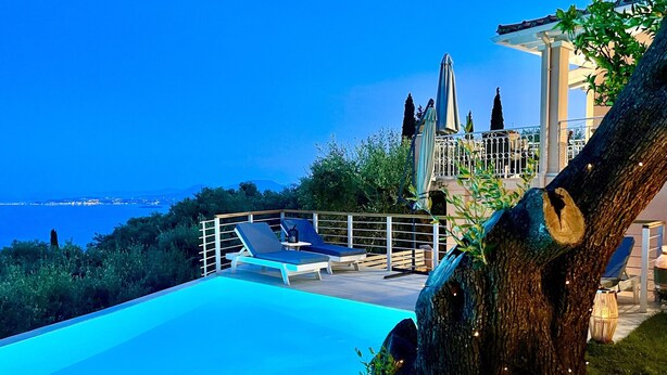 A pool area with lounge chairs, a tree with lights, and a view of the sea.