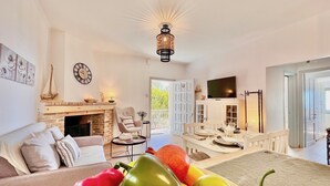 A living room with a fireplace, a sofa, a dining table set, and a fruit bowl.