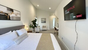 A modern hotel room with a large bed, a flat-screen TV mounted on the wall, a desk, and a chair. - Brand New Home* Dual Master Suites. (Boise)