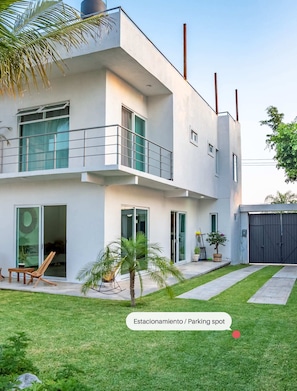 Ein modernes, zweistöckiges Haus mit Balkon, großen Fenstern und einem kleinen Garten.